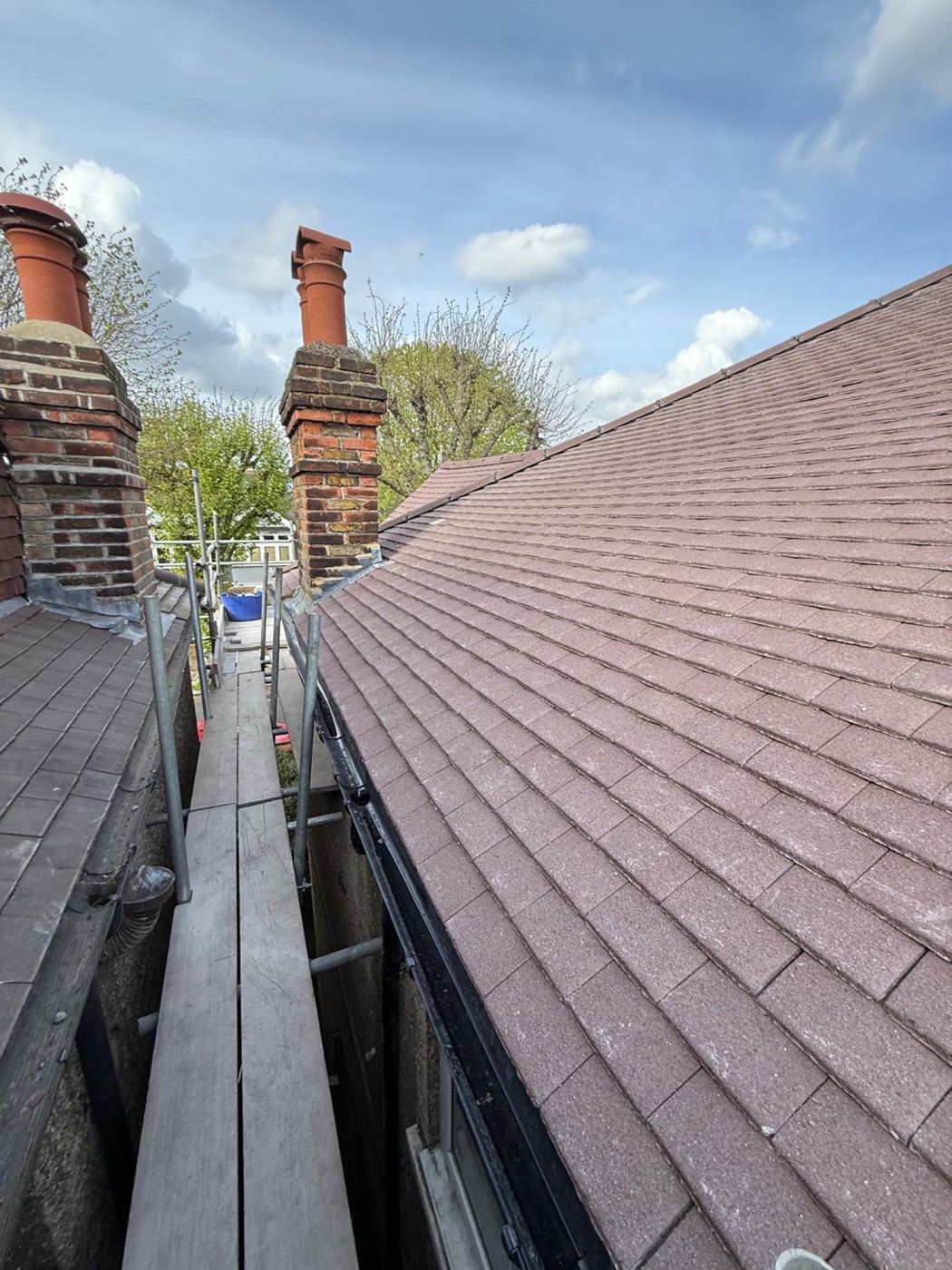New plain-tile slope along the scaffold run with the old brick chimney stacks repointed