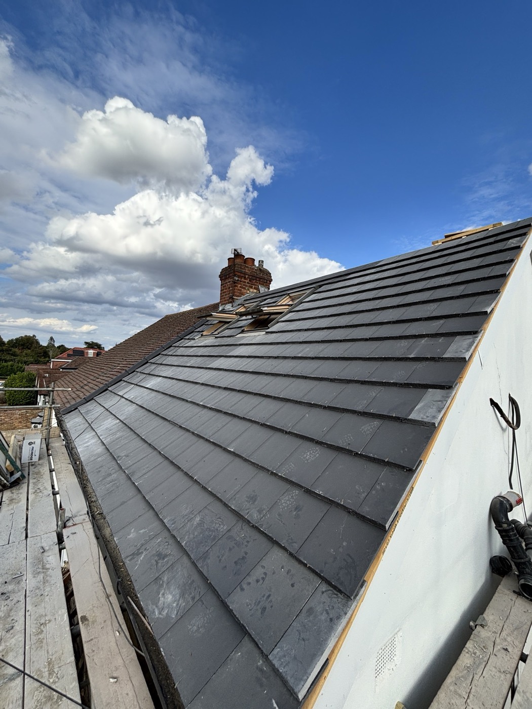 Finished slope of new dark grey interlocking tiles running up to the chimney